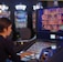 A person is seated at a slot machine console in a casino, focusing intently on the game displayed on the screen. The background shows several other illuminated gaming machines, adding a vibrant and colorful atmosphere to the scene.